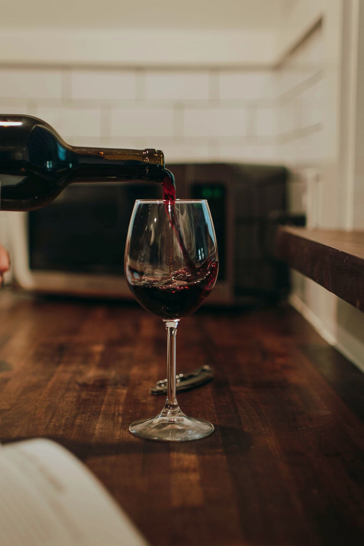 Rotwein wird aus Flasche in ein Glas in gemütlicher Küche eingeschenkt.