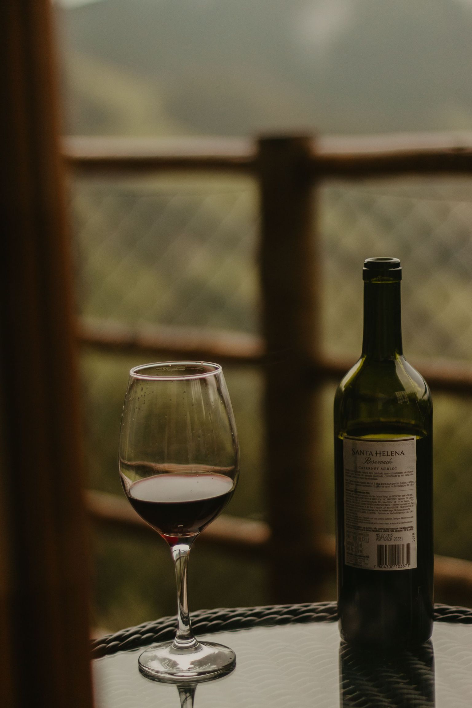 Glas mit Rotwein und Flasche auf Terrasse mit Aussicht.