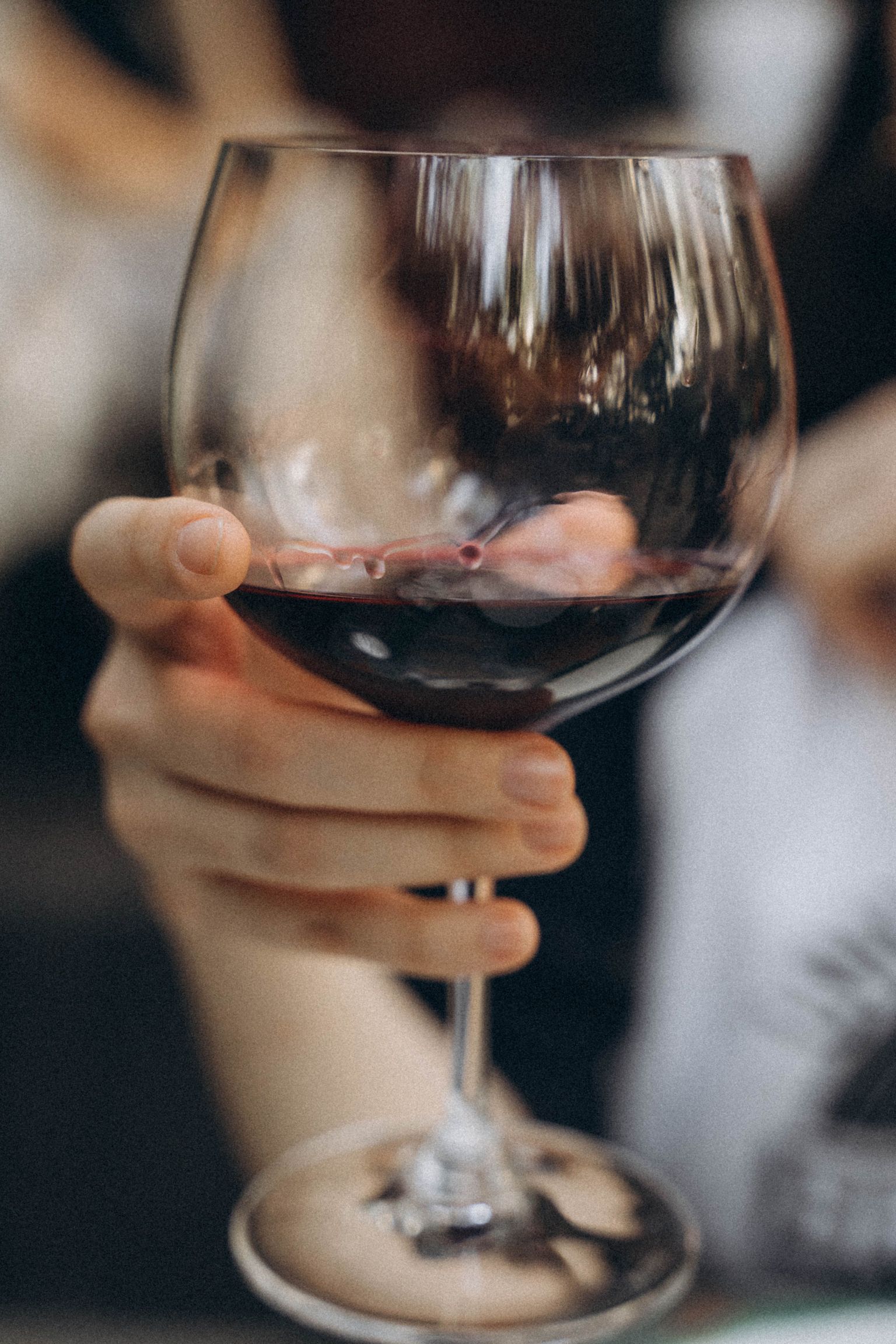 Person hält Weinglas mit rotem Wein und zwei Weintrauben am Stiel.