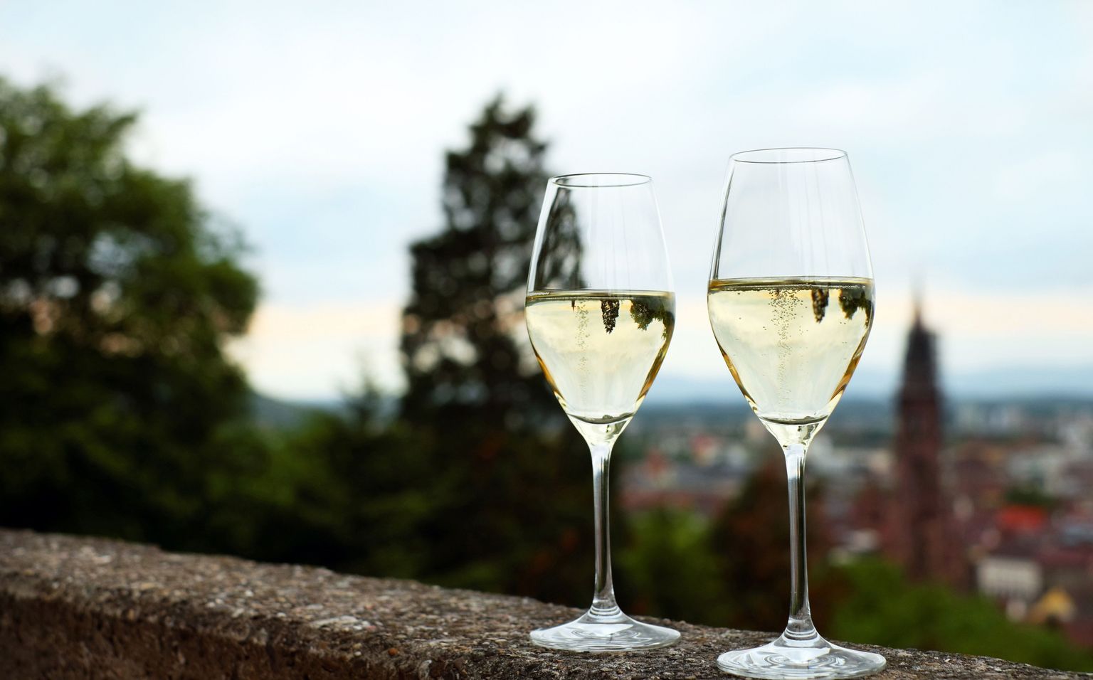 Zwei Weingläser mit Weißwein auf Mauer mit Panoramablick über eine Stadt.